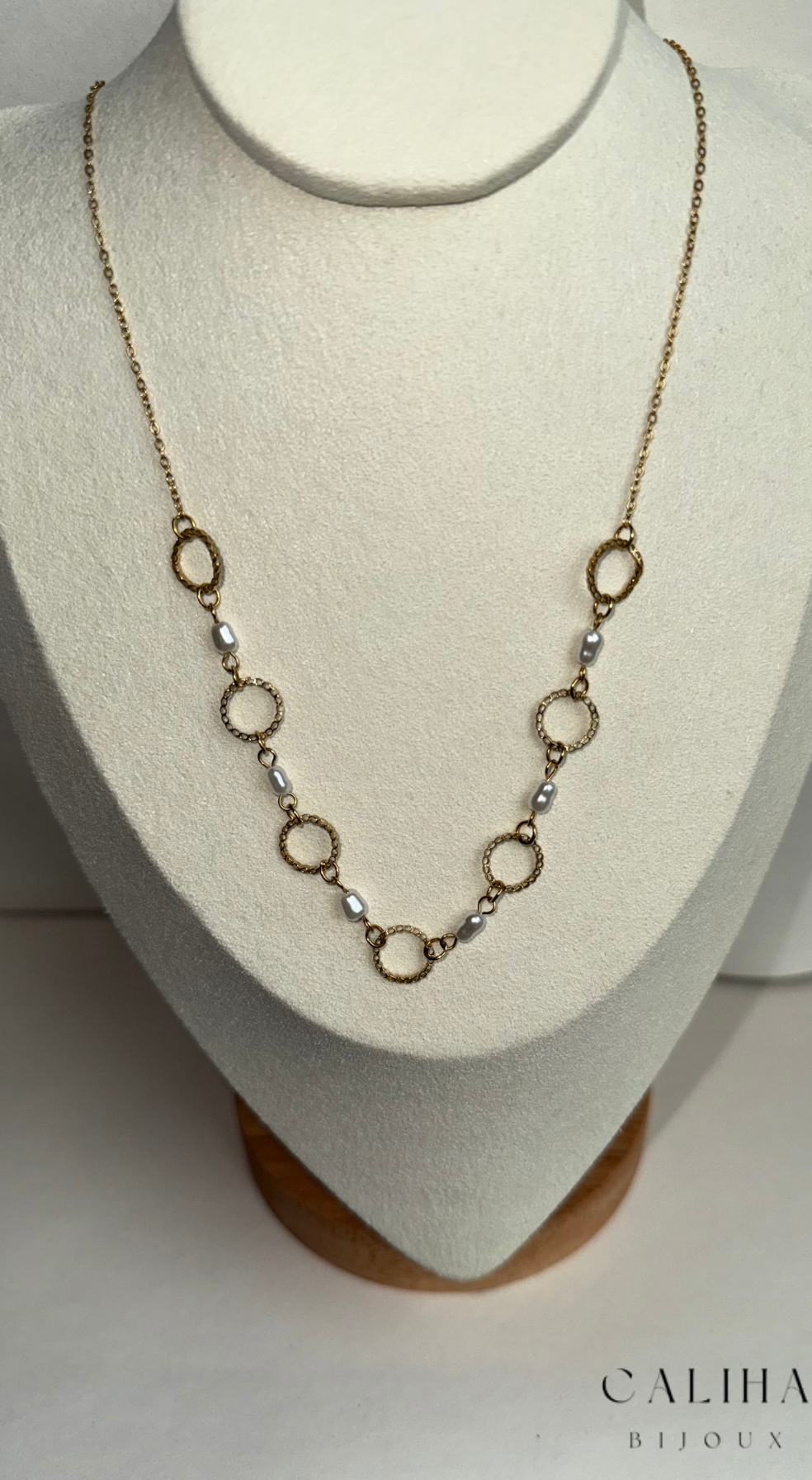 Collier doré composé de maillons circulaires et de perles blanches, délicatement présenté sur un bustier blanc – Bijou élégant et raffiné
