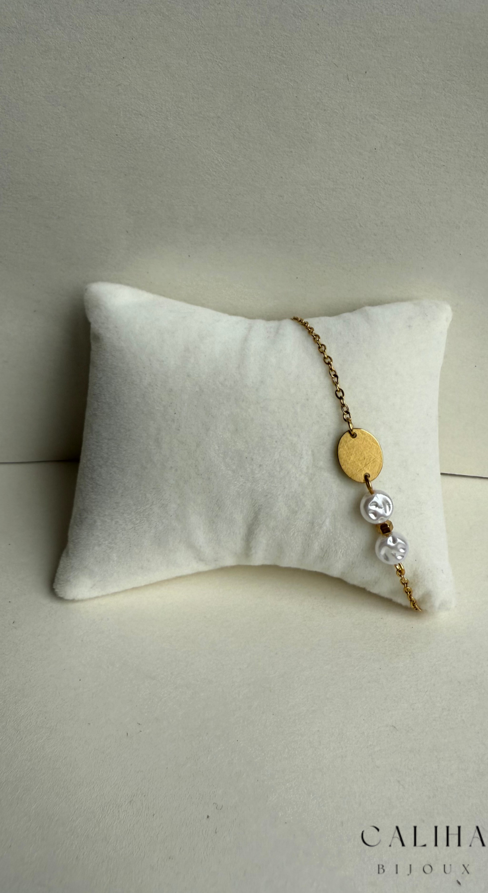 Vue latérale du bracelet doré avec perles blanches et un élément ovale doré, présenté sur coussin blanc – Design moderne et délicat